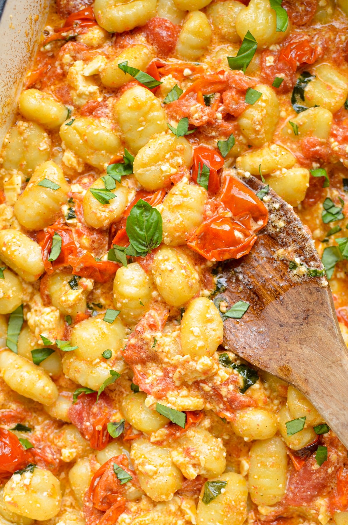 A close up of baked feta and gnocchi pasta, garnished with basil.