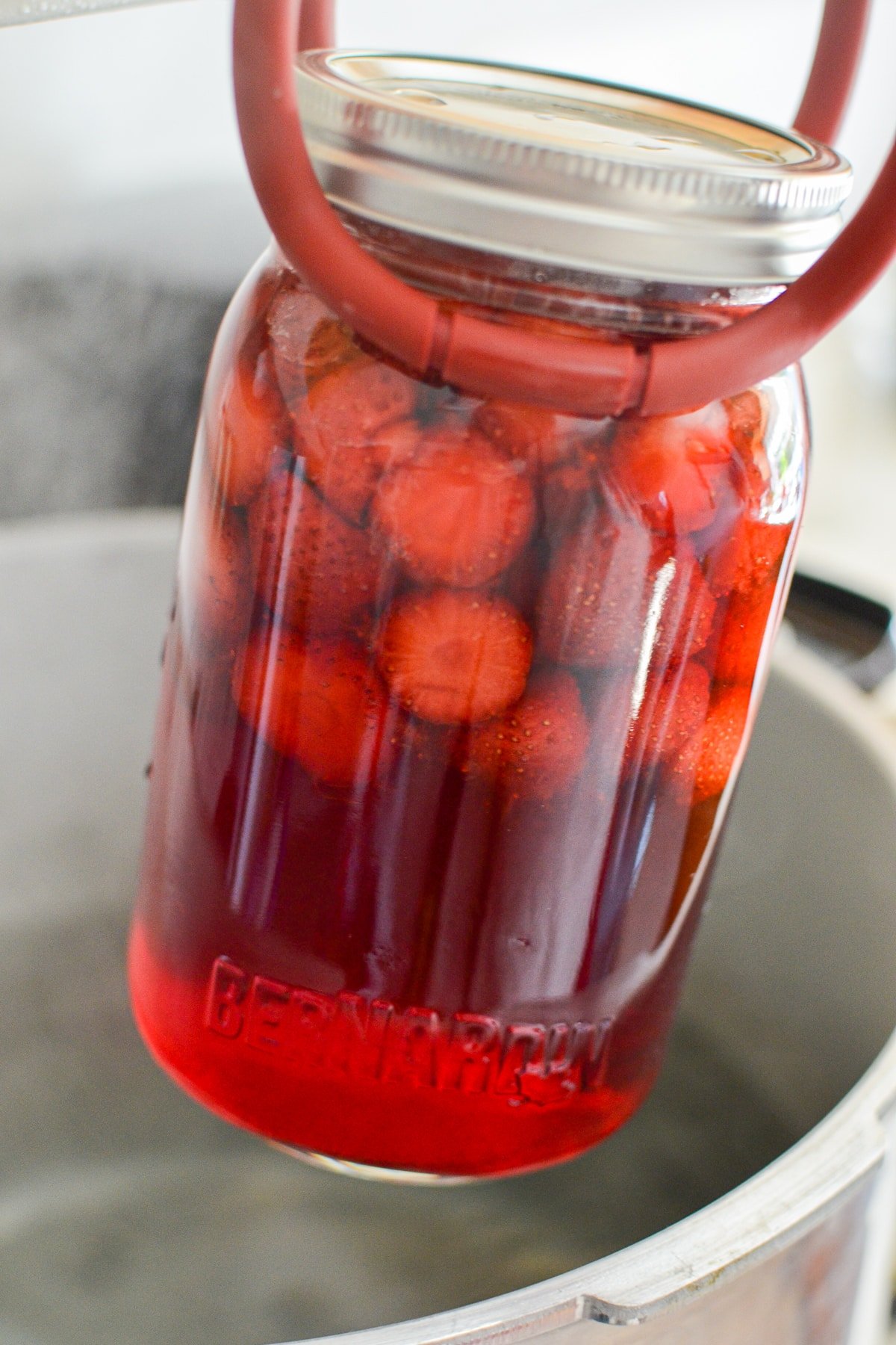 Transferring a jar of strawberries into a canner.