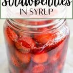 A tall jar of strawberries in syrup.
