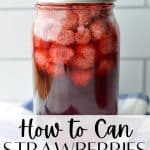 A tall jar of strawberries preserved in syrup.