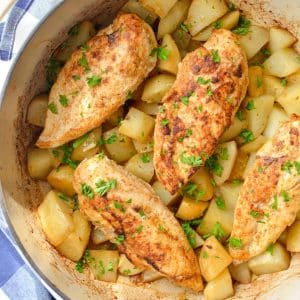 Four chicken breasts on top of a layer of cubed potatoes in a Dutch Oven.