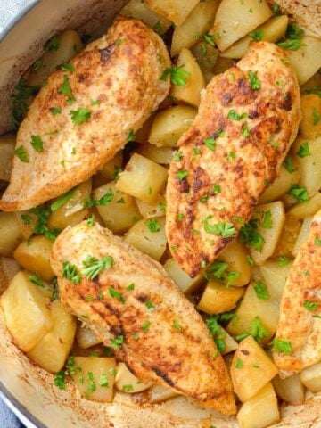 Four chicken breasts on top of a layer of cubed potatoes in a Dutch Oven.