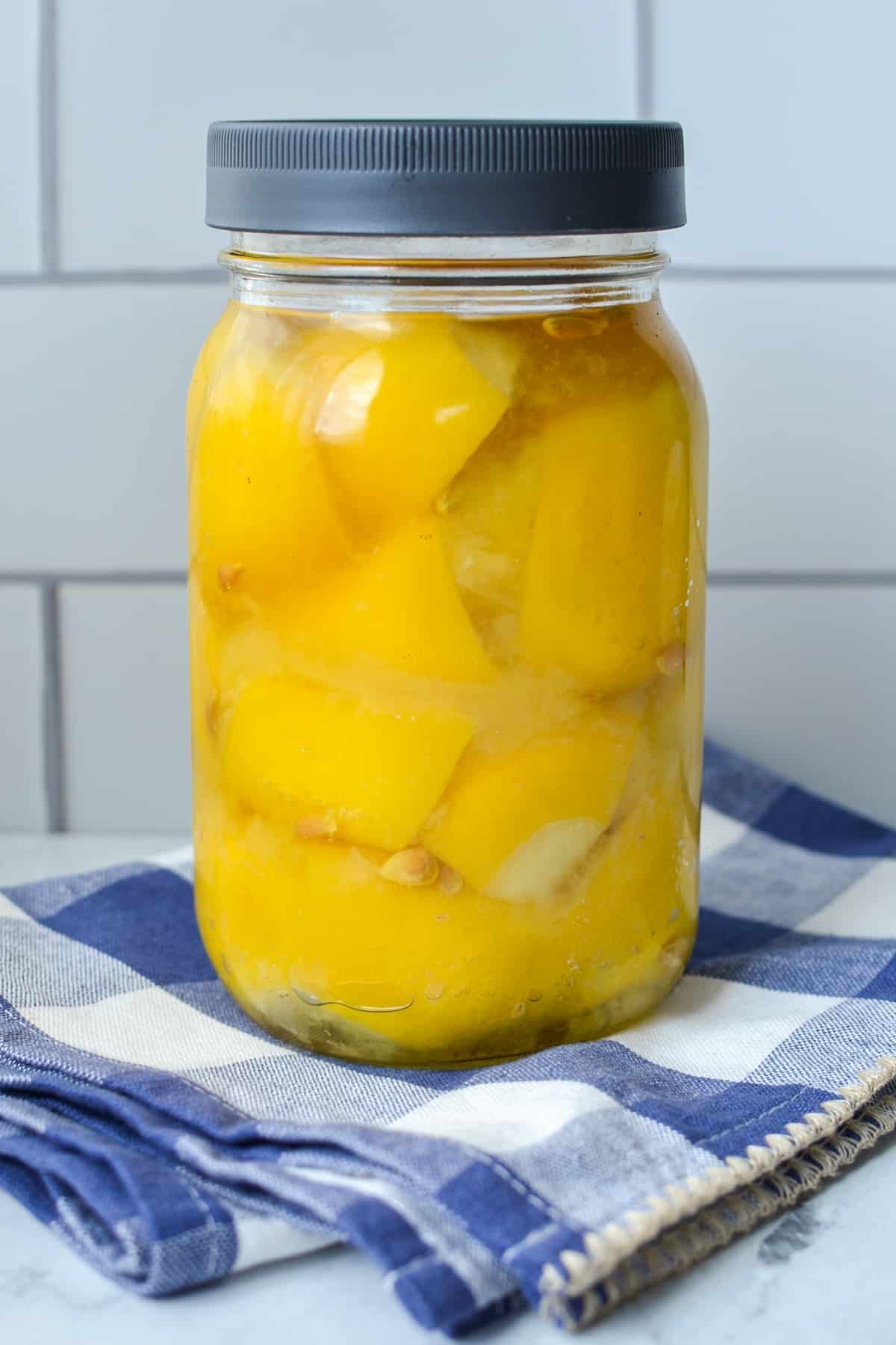 A jar of fermented lemons on a blue check napkin.