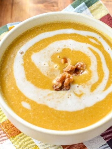 A bowl of butternut squash soup with a swirl and garnished with candied walnuts.