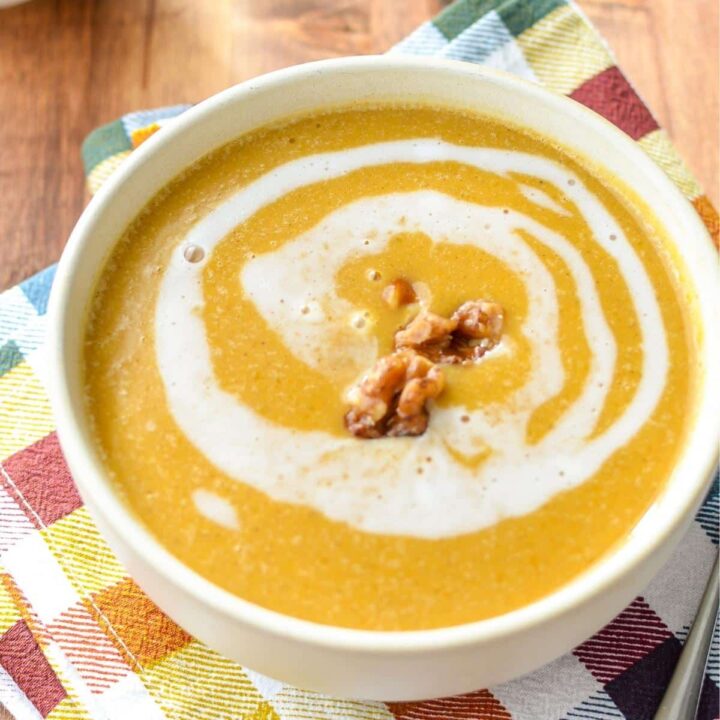 A bowl of butternut squash soup with a swirl and garnished with candied walnuts.