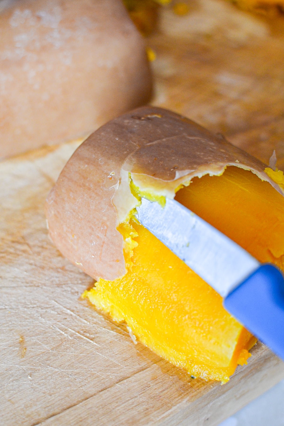 Using a paring knife to remove the skin from a partially cooked butternut squash.