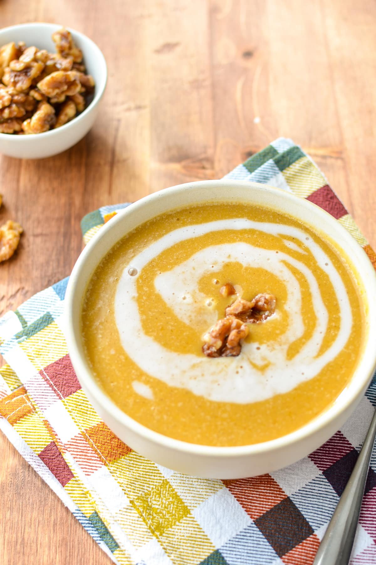 A bowl of butternut squash soup, garnished with a coconut milk swirl and candied walnuts.