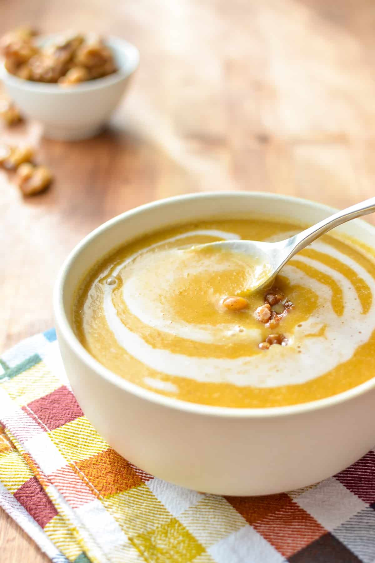 A bowl of butternut squash soup with a spoon taking out a portion.