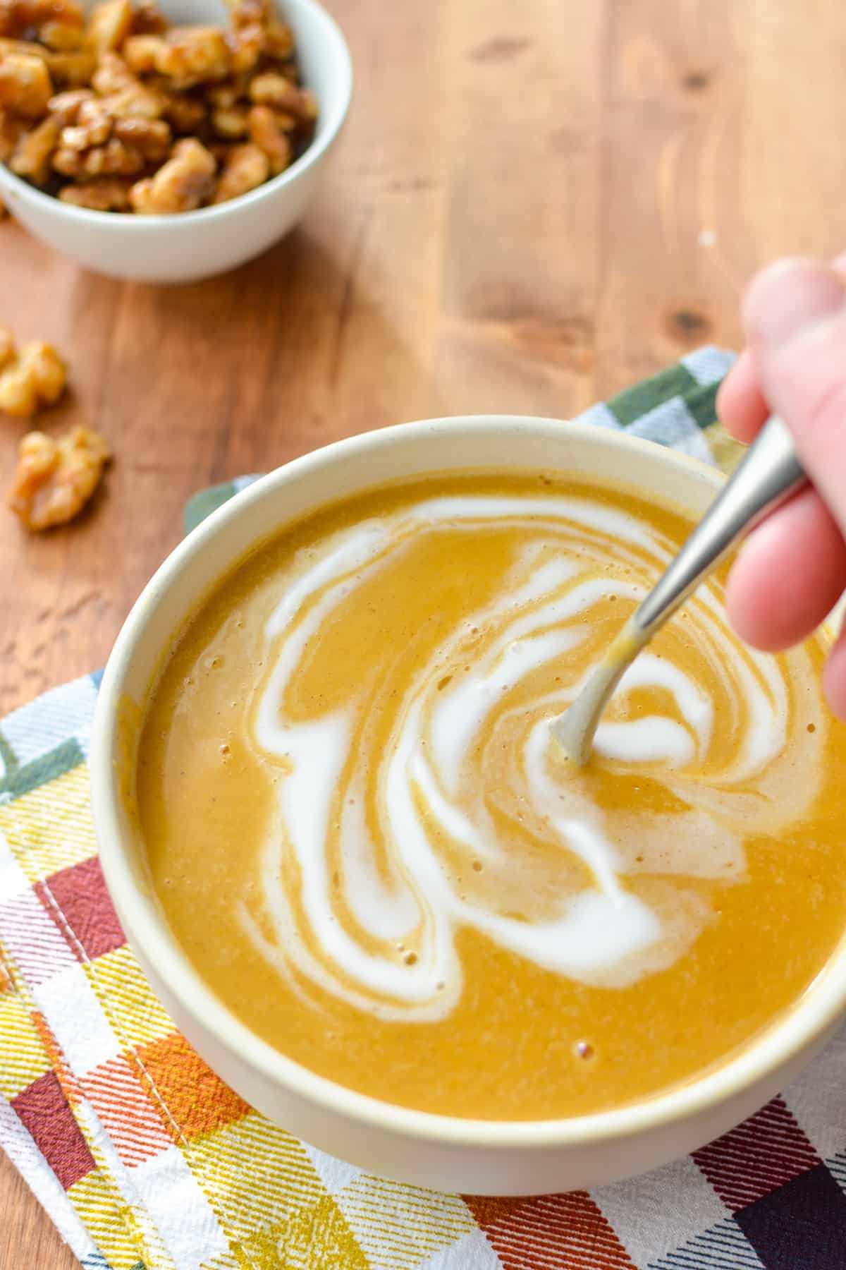 A hand stirring a spoon in a bowl of butternut squash soup.