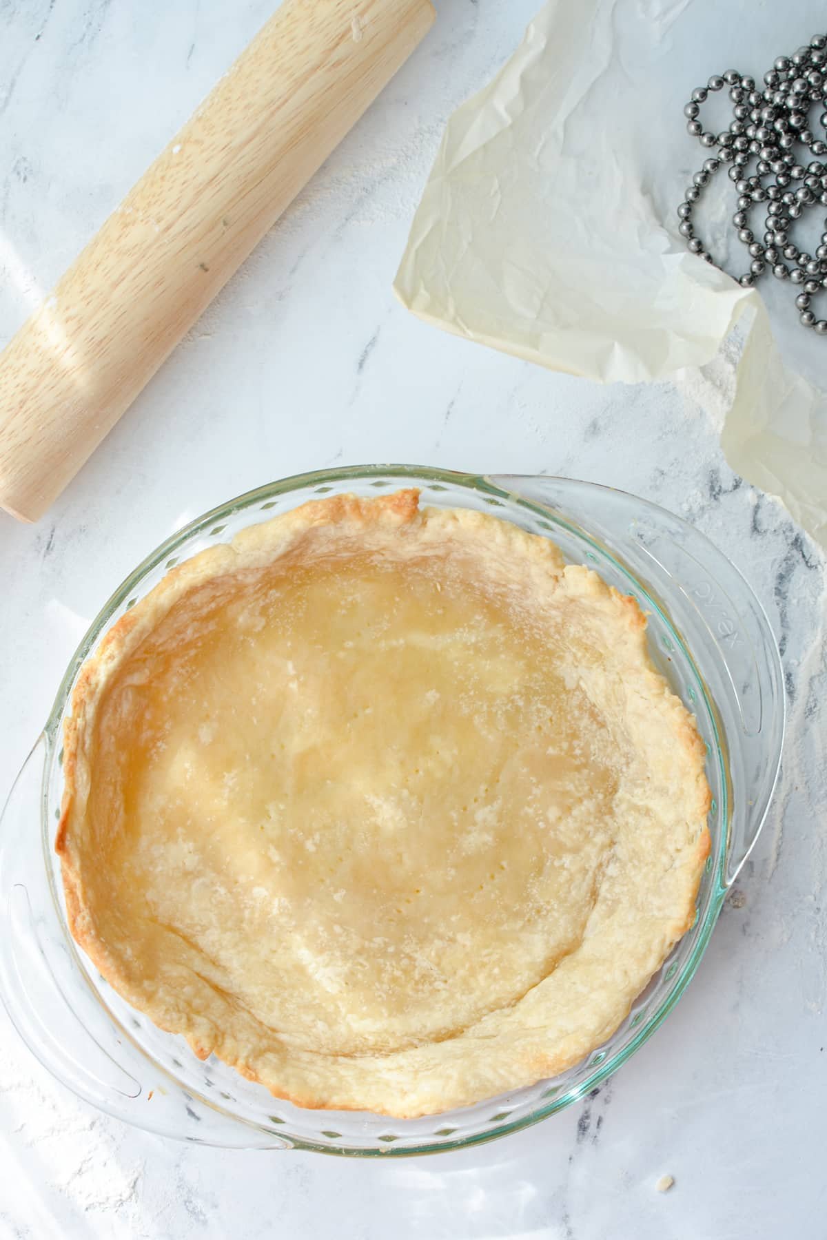 An overhead shot of a partially baked pie crust with a rolling pin in the corner.