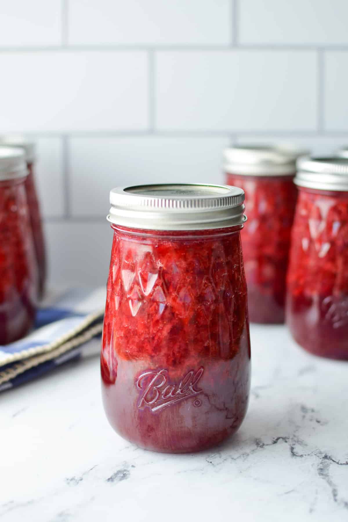 Several jars of strawberry jam on a white marble surface.