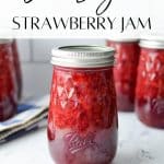 A jar of homemade strawberry jam on a white marble surface.