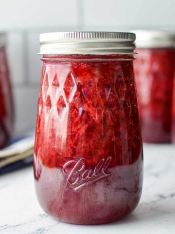 A jar of strawberry jam in a tapered jar.