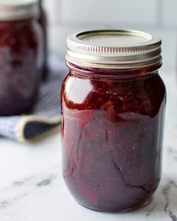 A jar of homemade jam on a white marble surface.