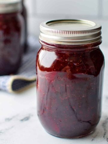 A jar of homemade jam on a white marble surface.