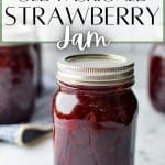 A jar of strawberry jam on a marble surface.