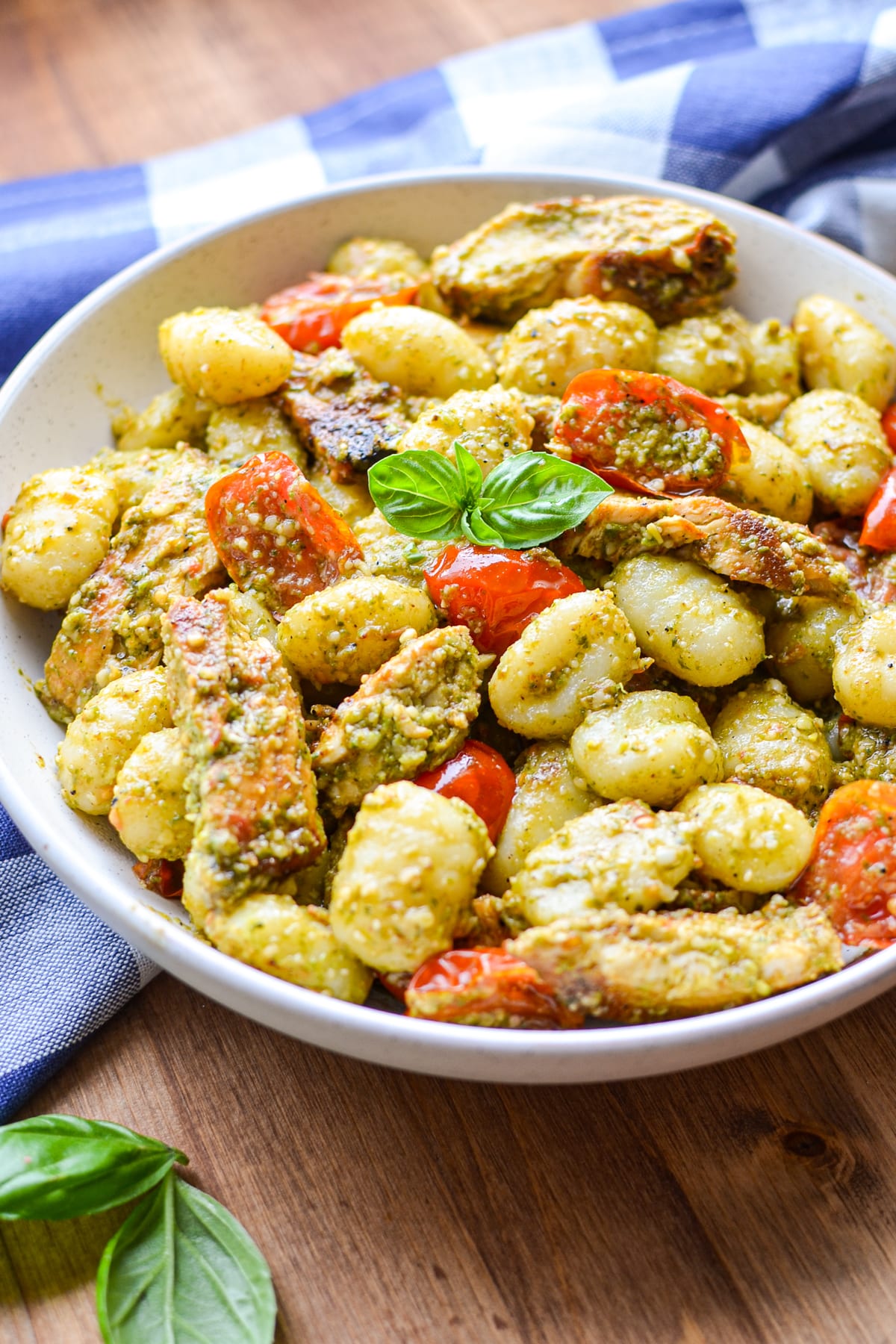 A bowl of gnocchi tossed with pesto and garnished with basil.