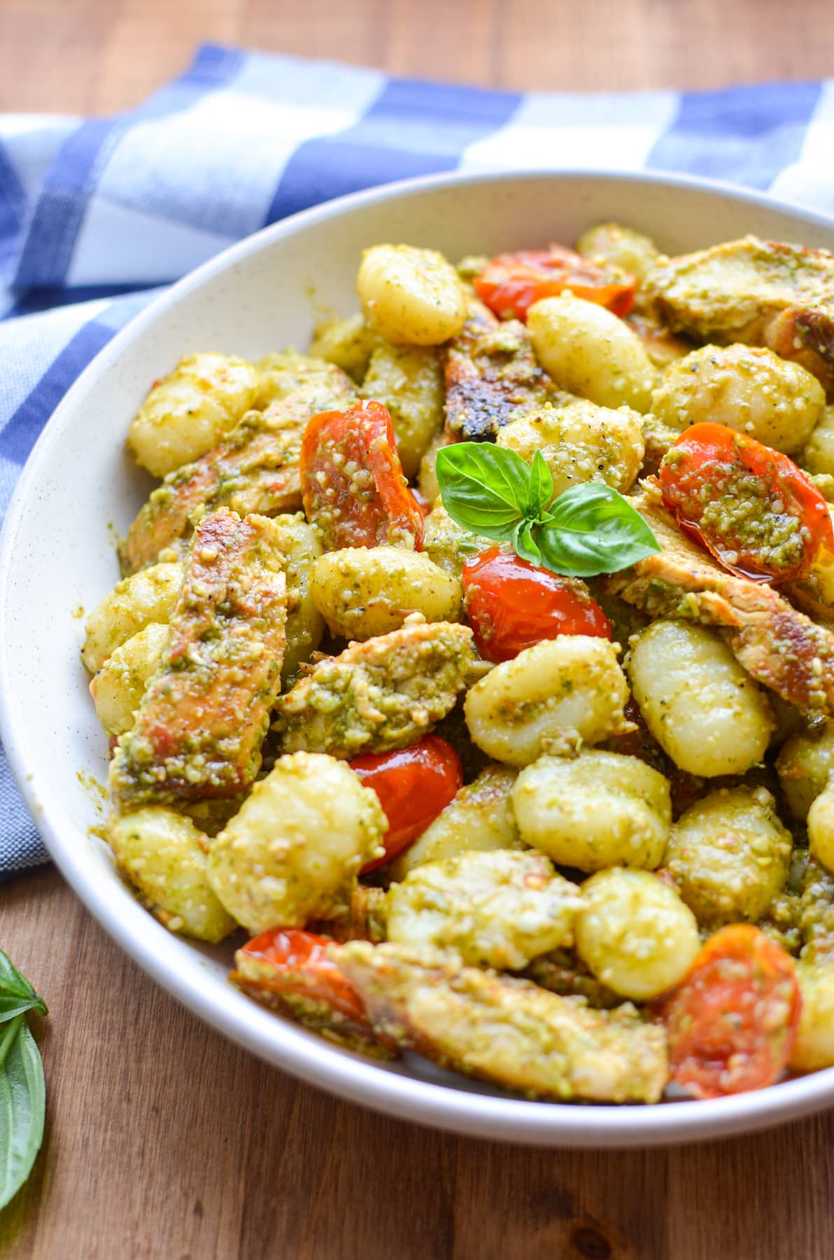 A bowl of gnocchi tossed with pesto and garnished with fresh basil.