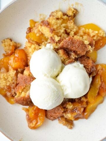 A plate of peach cobbler, served with three scoops of vanilla ice cream.