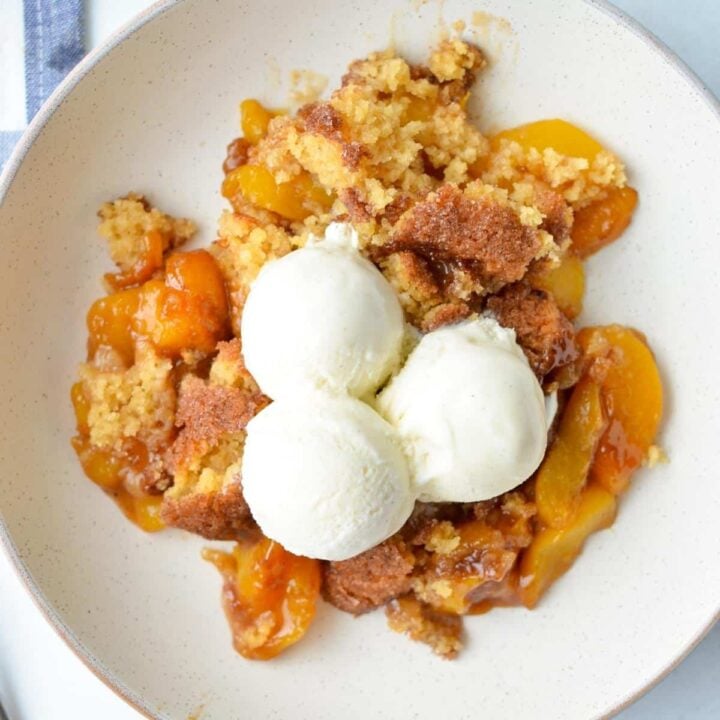 A plate of peach cobbler, served with three scoops of vanilla ice cream.