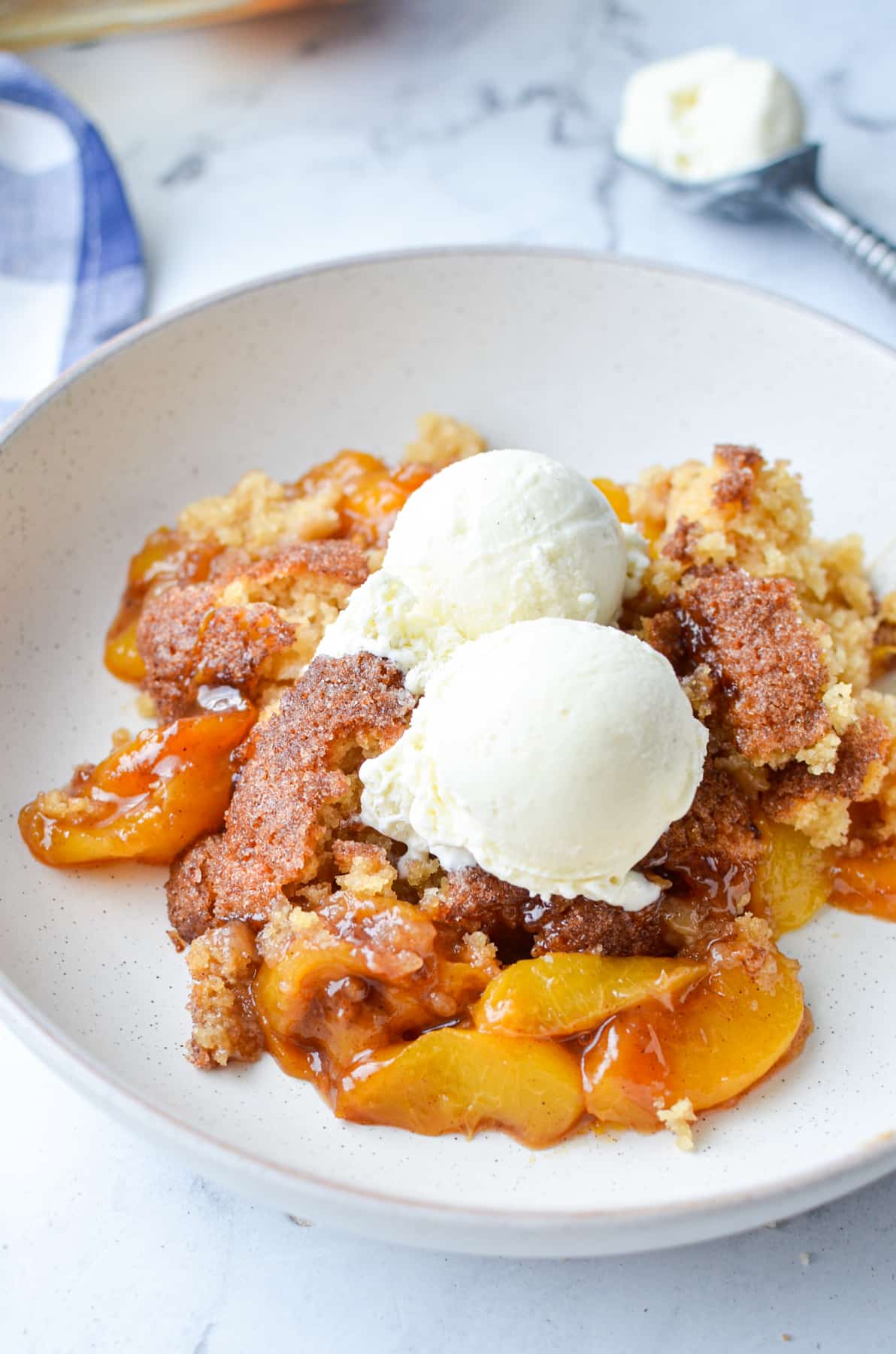 A shallow bowl of peach cobbler served with ice cream.