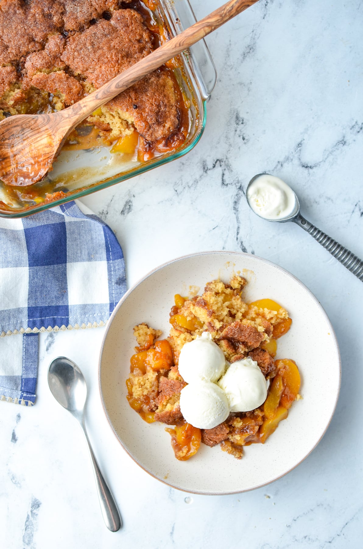 An overhead view of a serving of peach cobbler with ice cream, with the baking dish in the corner.