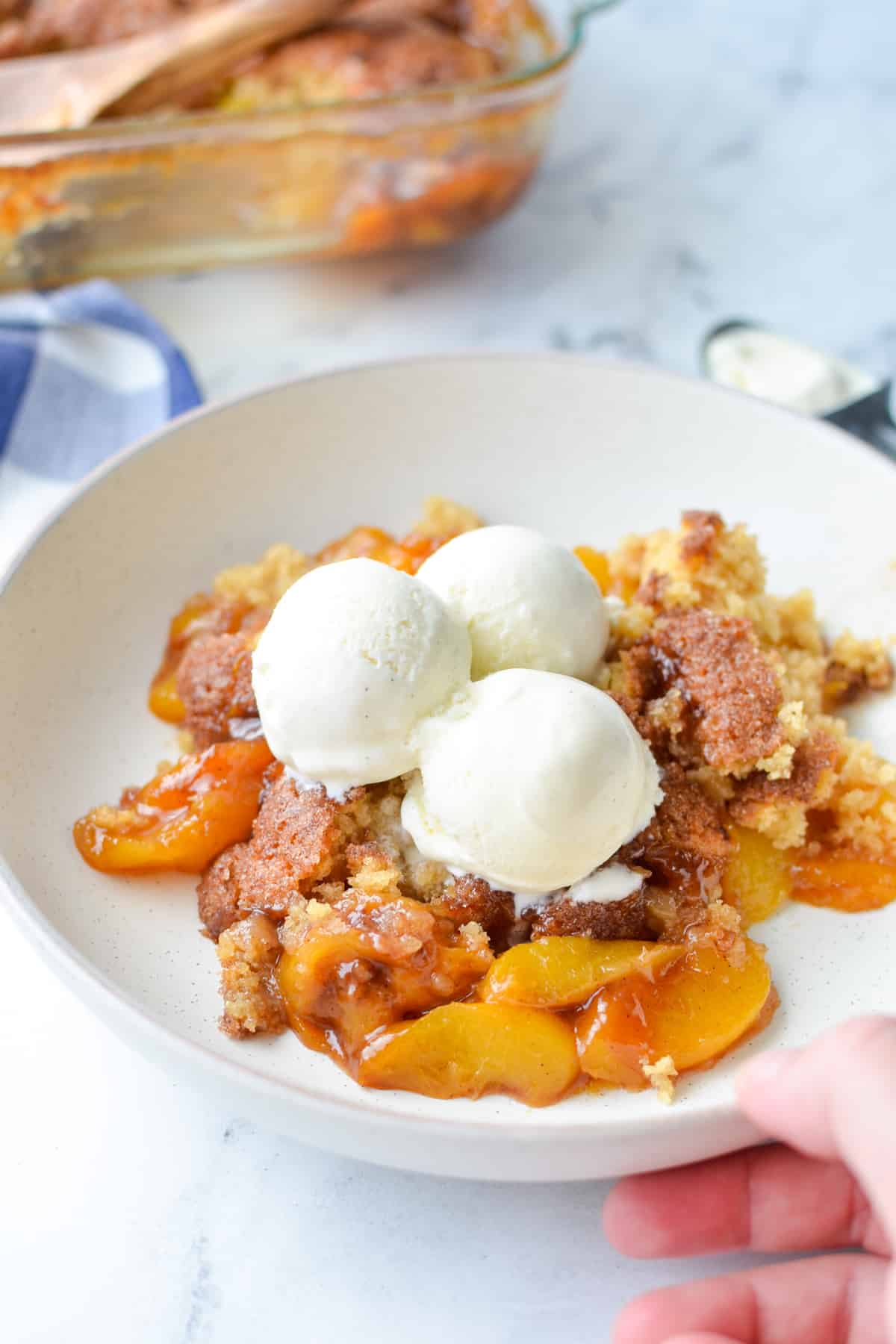 A serving of sourdough peach cobbler with several scoops of vanilla ice cream.