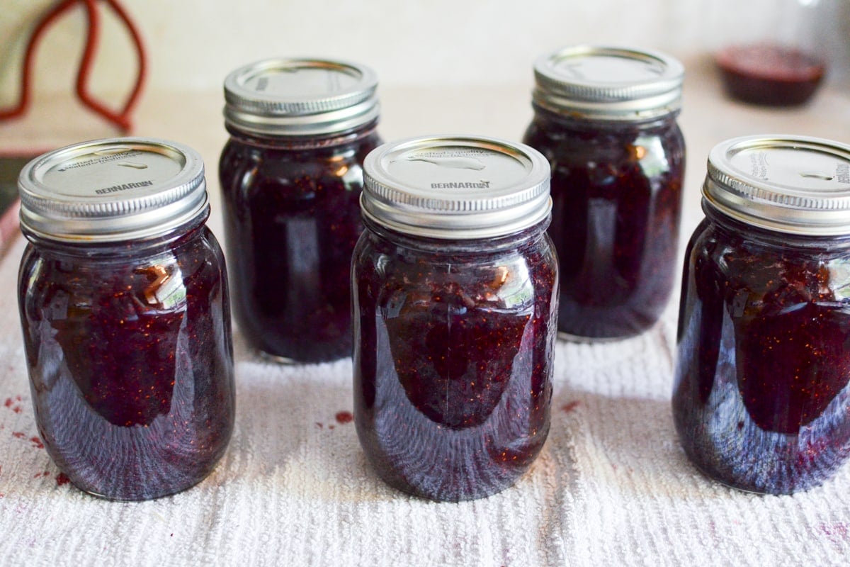 Jars of jam on a white cloth on a counter.