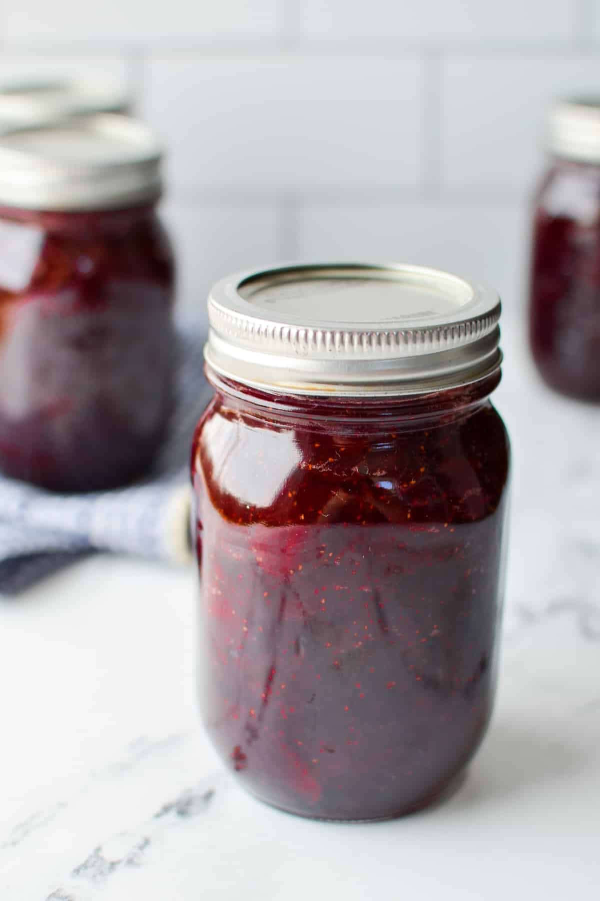 A jar of strawberry jam on a counter, with others in the background.