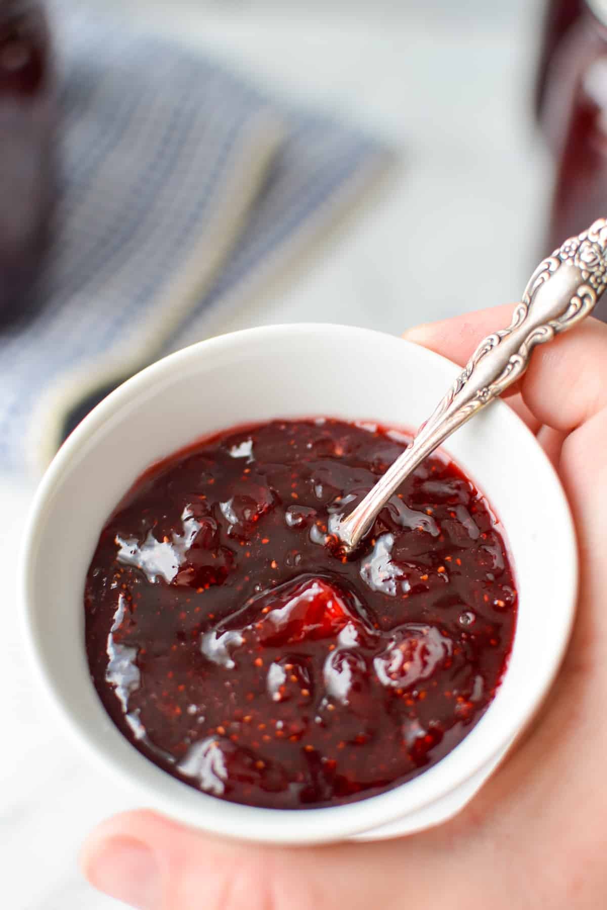 A small amount of homemade jam in white dish with a small spoon in it.