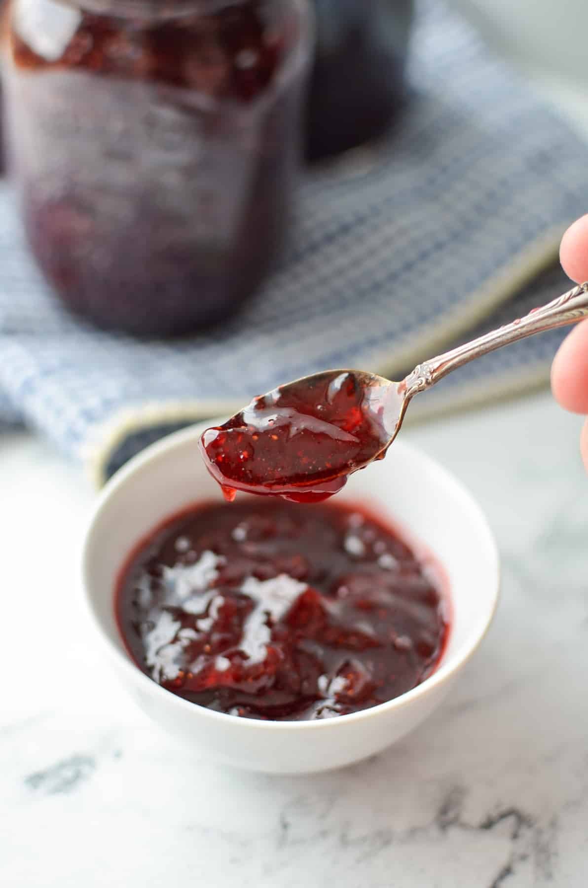 A small white bowl with jam and a small spoon in it.