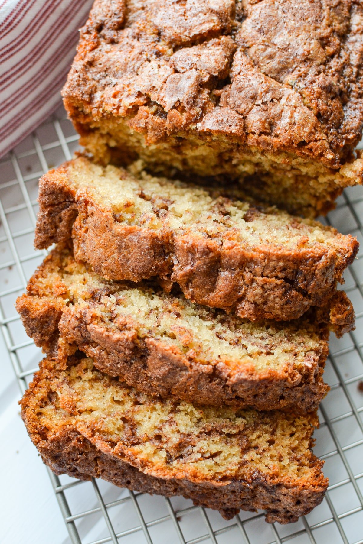 A loaf of cinnamon bread on a cooling rack, cut into thick slices.