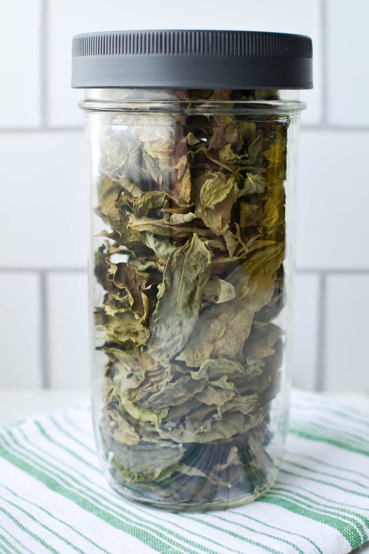Adding dried basil to a glass jar.