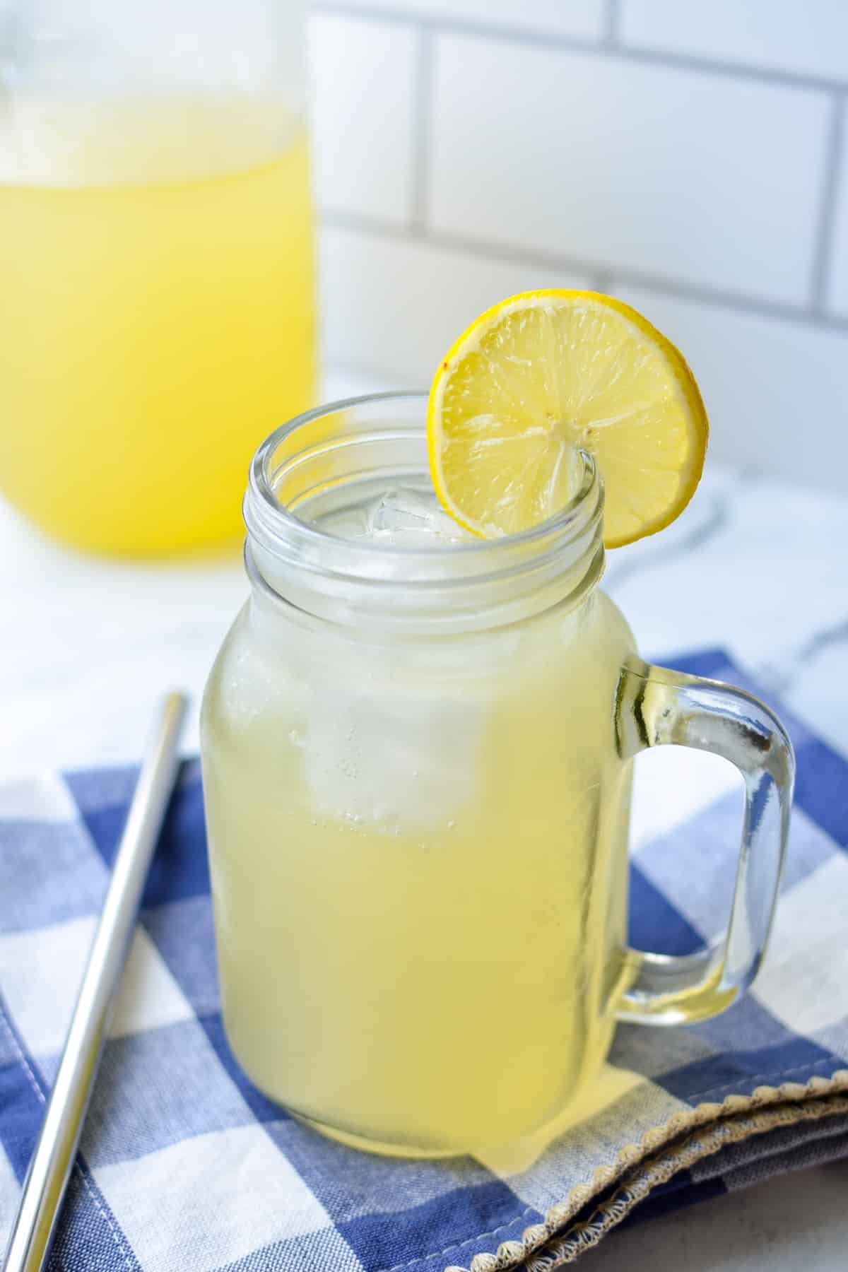 A handled mason jar with a lemon based beverage in it, served over ice with a lemon wedge.