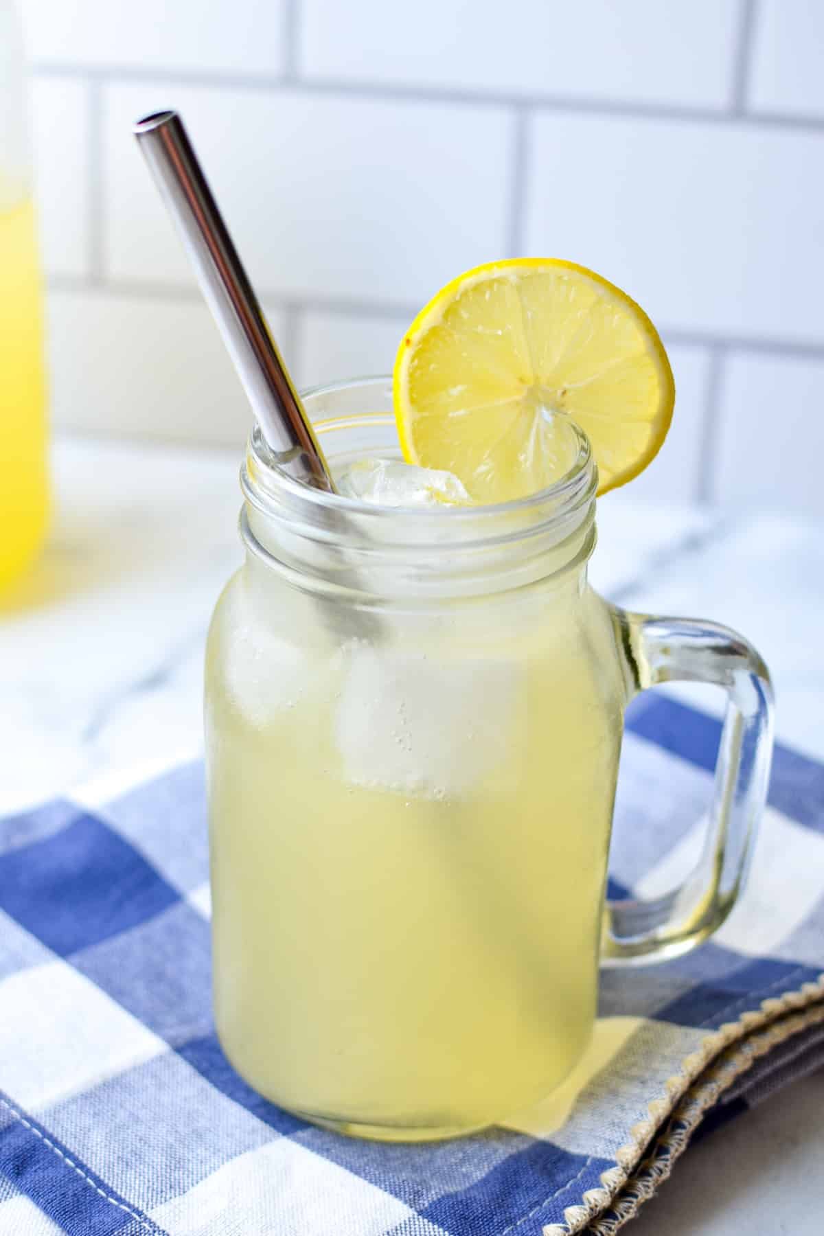 A handled mason jar cup with a lemon beverage, served over ice with a lemon slice.