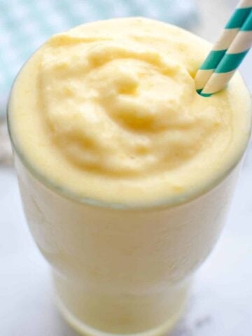 A close up of a glass of mango smoothie with a straw.