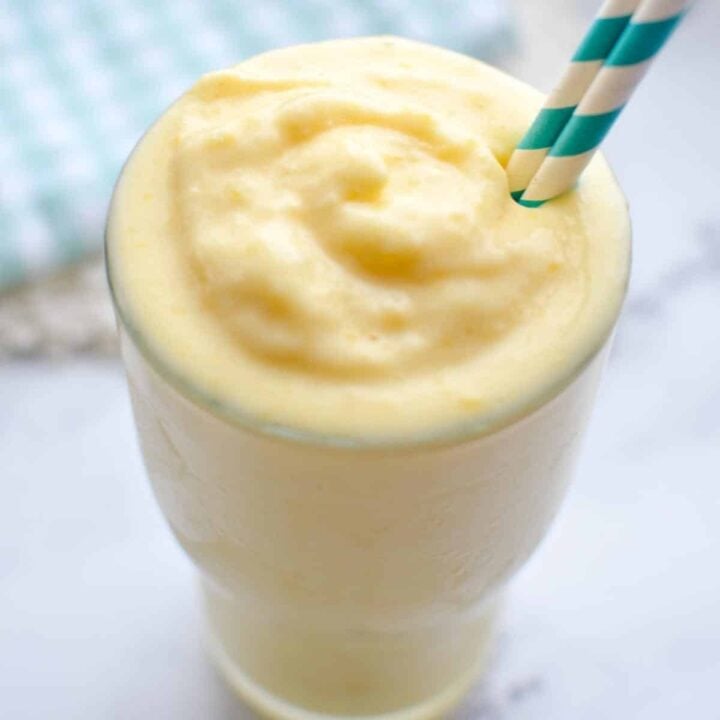 A close up of a glass of mango smoothie with a straw.
