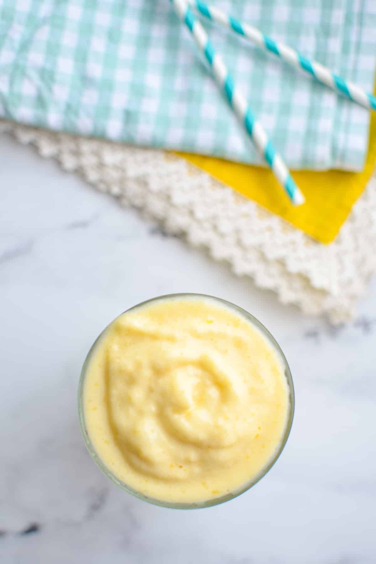 A glass of mango smoothie on a white marble background.