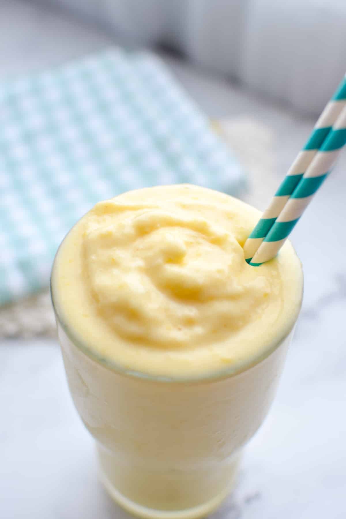 A glass of mango smoothie with a straw in it.