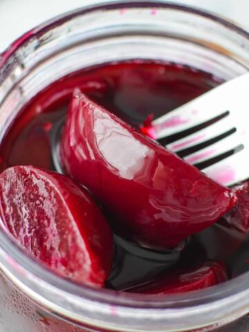 A fork removing a pickled beet from a jar.