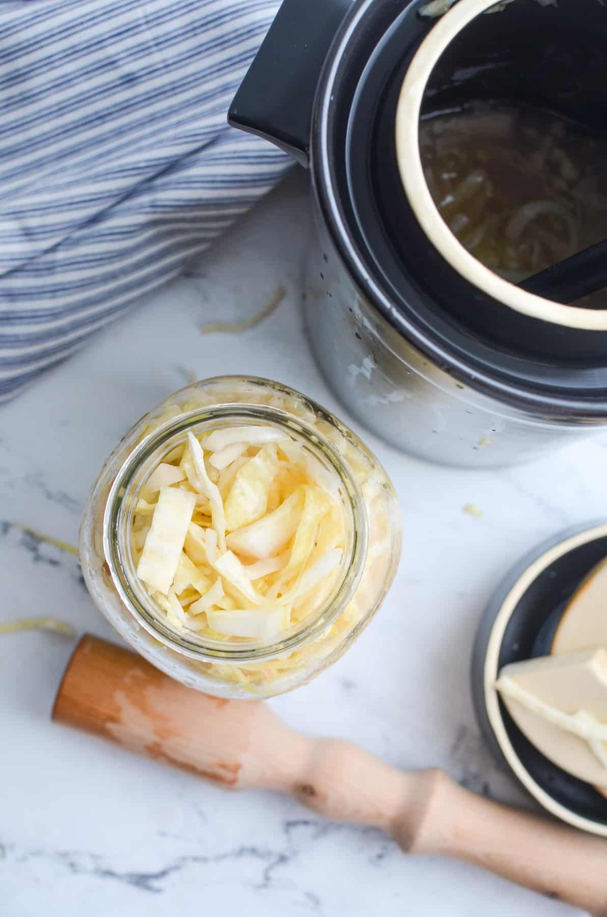 An overhead view of a jar of sauerkraut next to a fermentation crock.