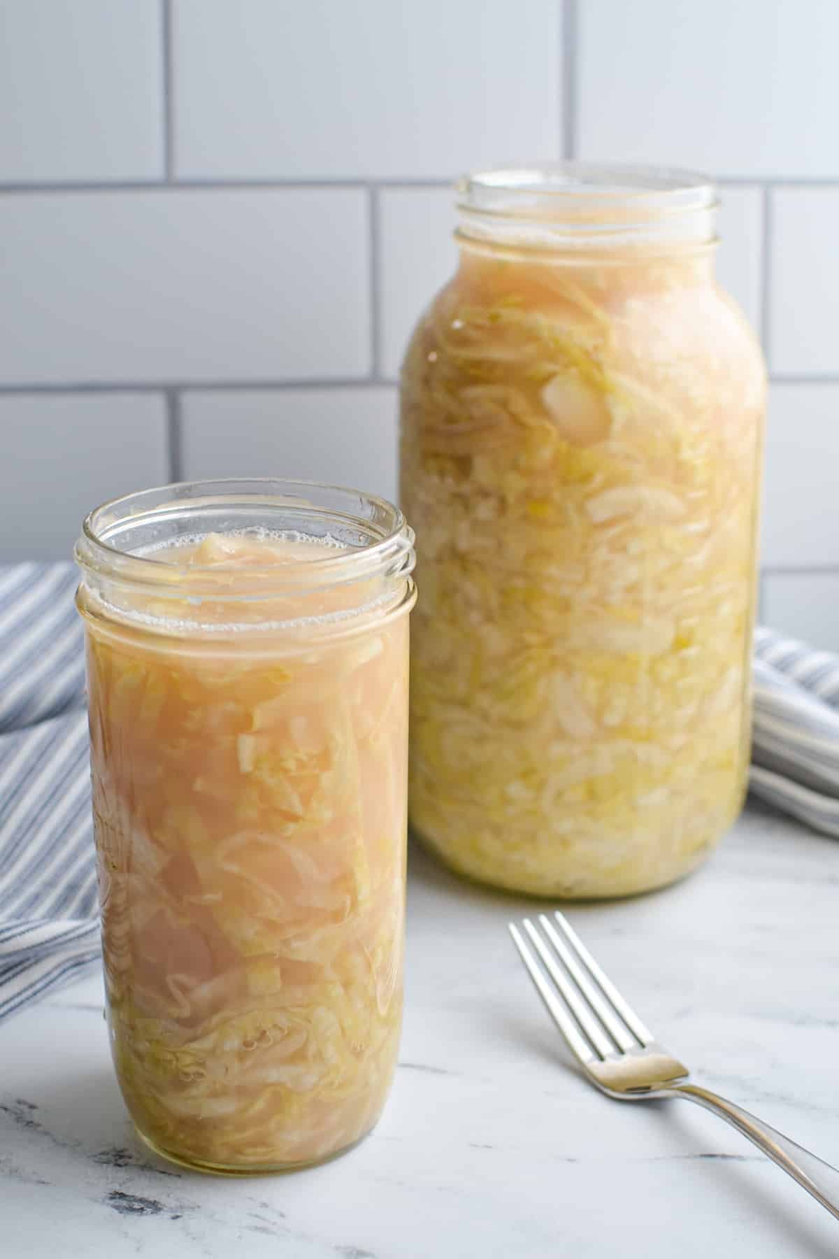 Two jars of sauerkraut on a marble countertop.
