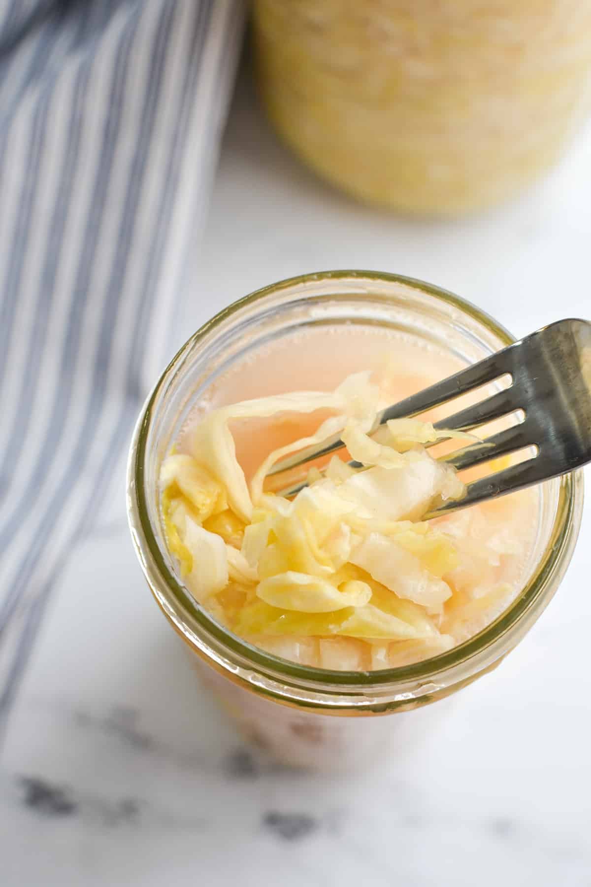 A fork taking a portion of sauerkraut from a jar.