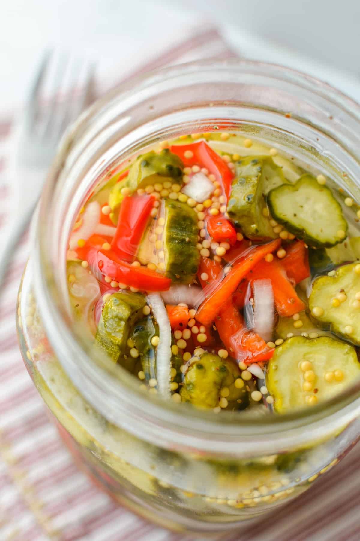 A jar filled with peppers, cucumbers, and onions in a brine.