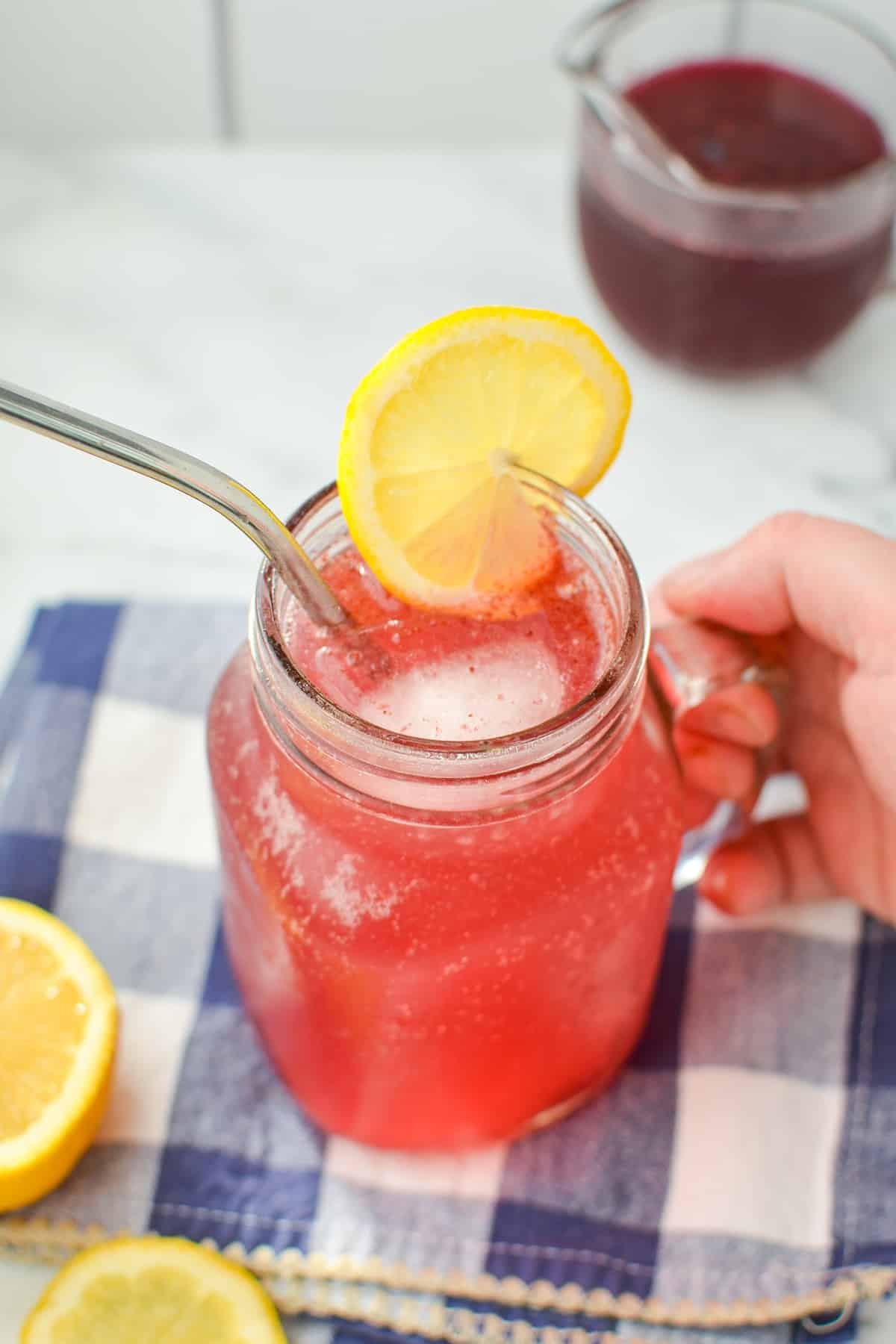 A glass jar filled with a blueberry cocktail and garnished with lemon.