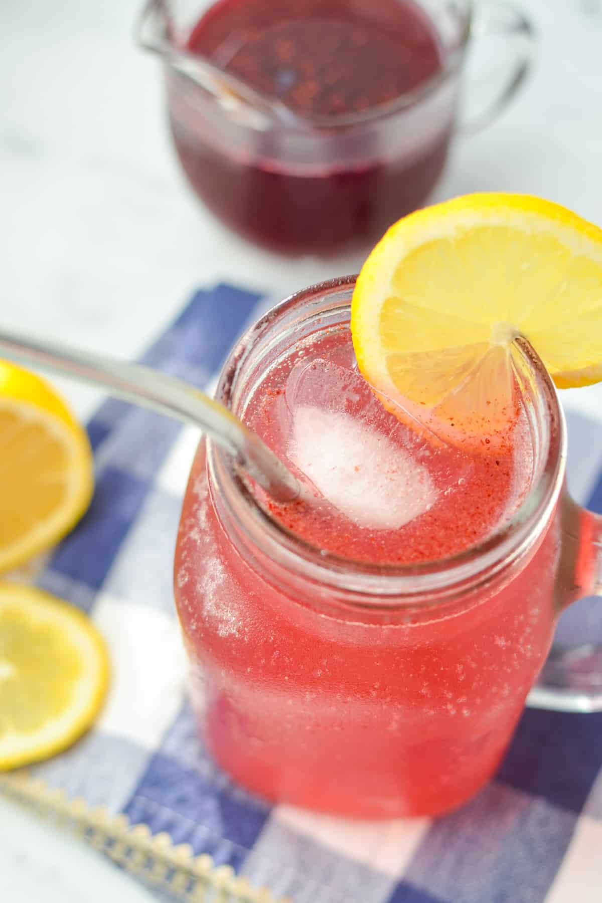 A glass jar with a blueberry shrub cocktail inside, garnished with lemon.