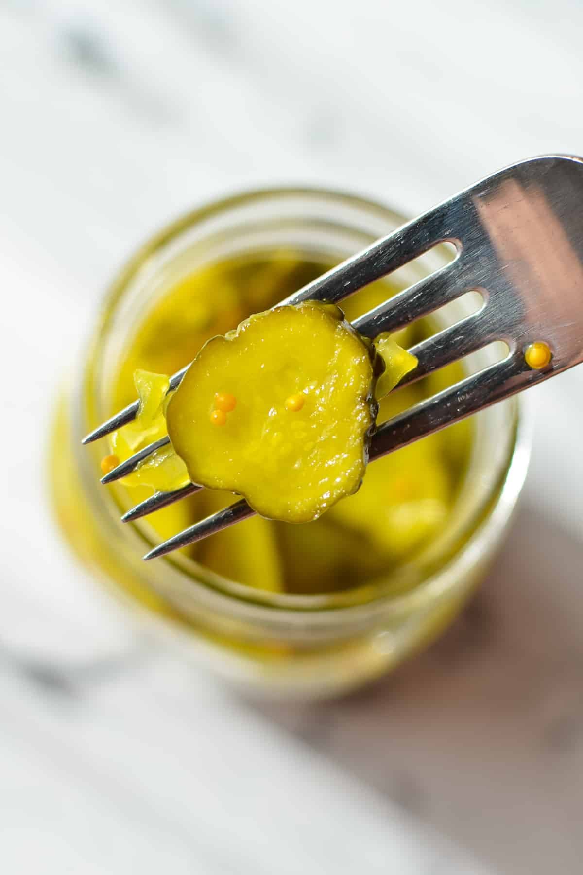 Using a fork to remove a pickled cucumber slice from a jar.