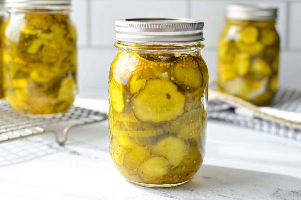 A close up of a jar of sweet pickles on a marble surface with others in the background.