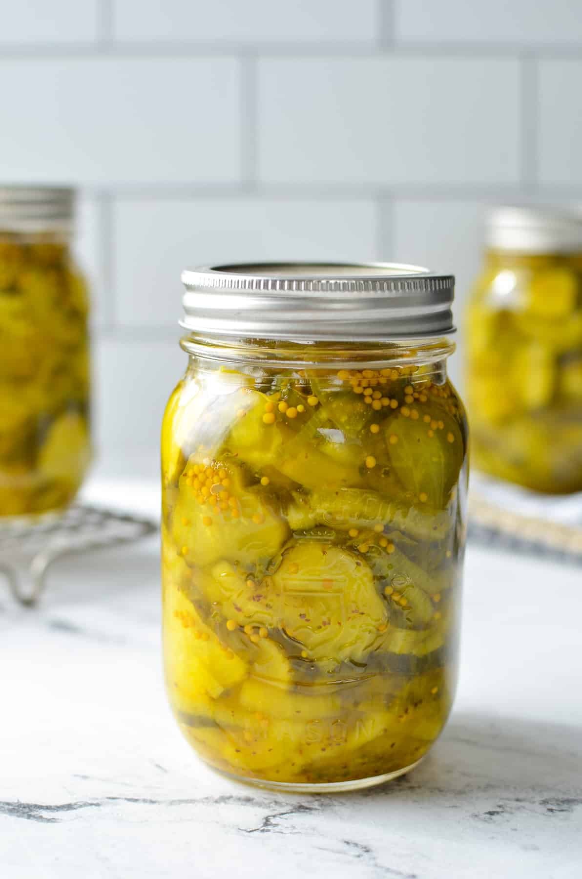 A jar of finished bread and butter pickles on a marble counter.