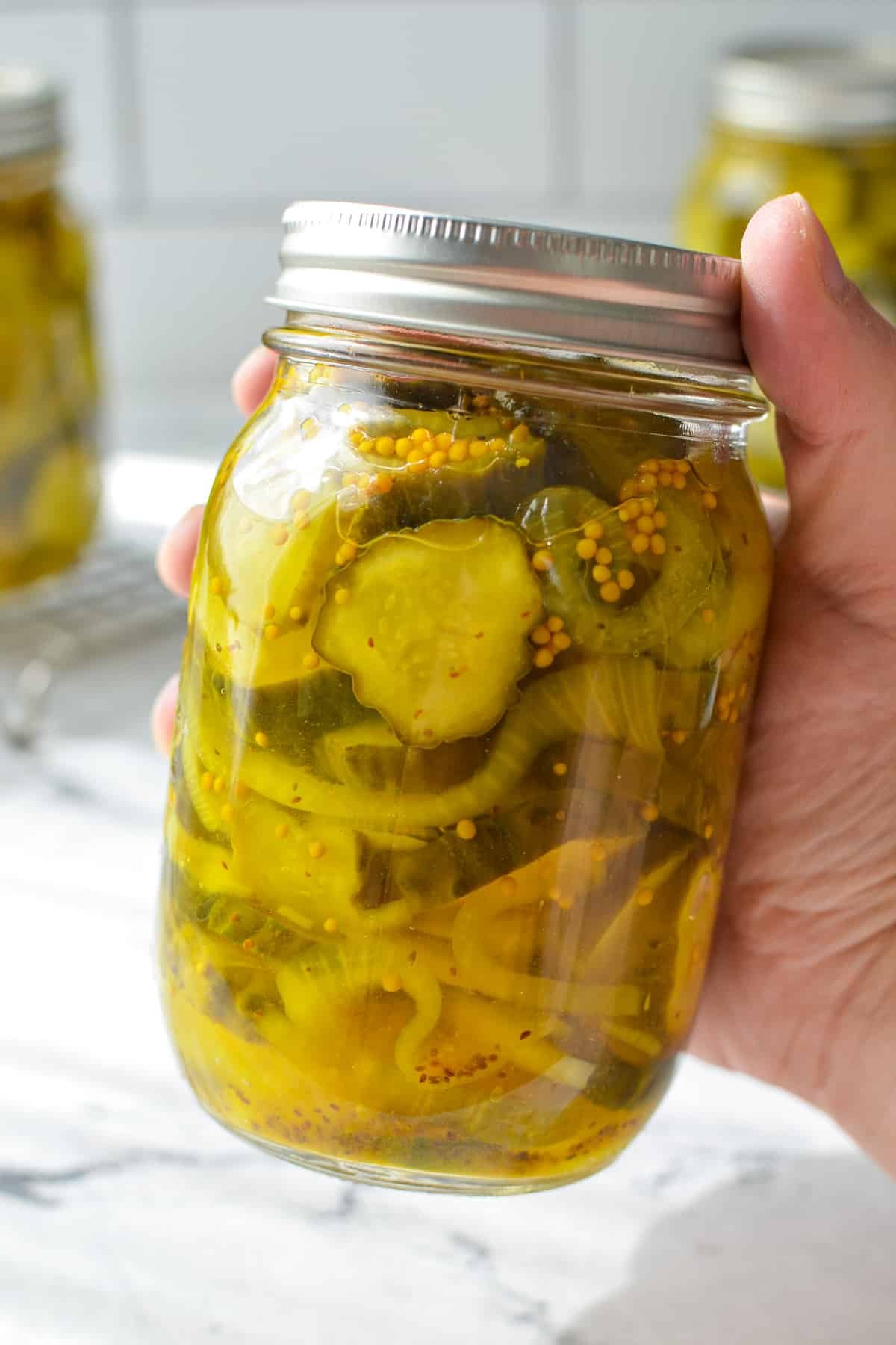 A jar of bread and butter pickles being held.